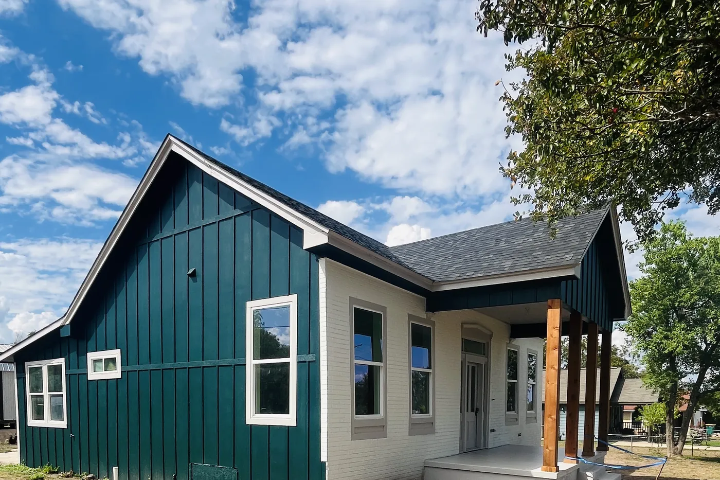 A renovated cottage with teal board-and-batten siding and a covered front porch