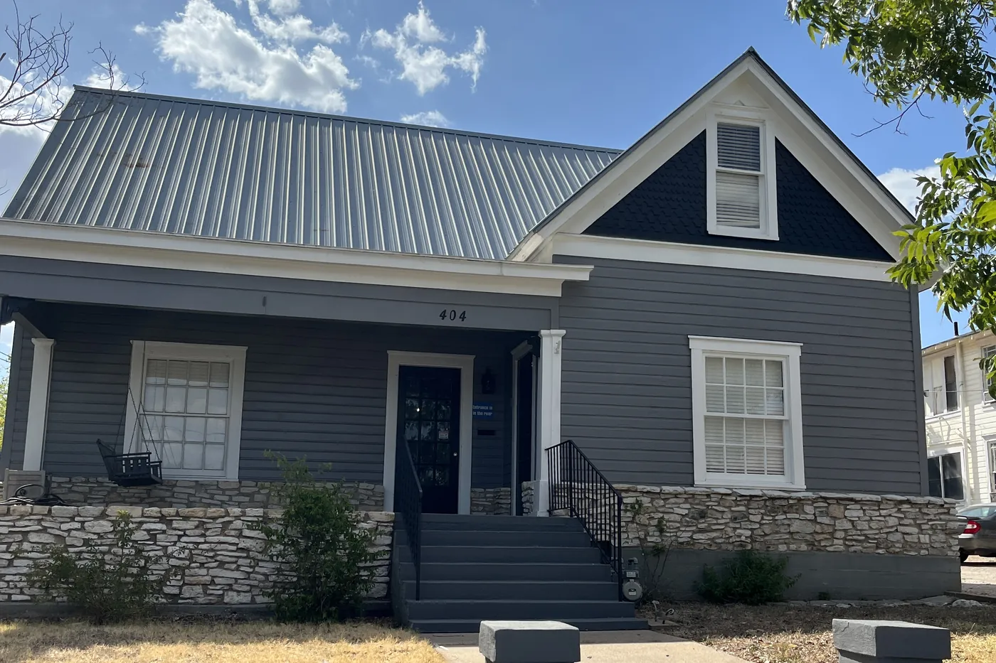 A renovated craftsman home in Belton with navy siding, a standing-seam metal roof and a stone-pillared porch